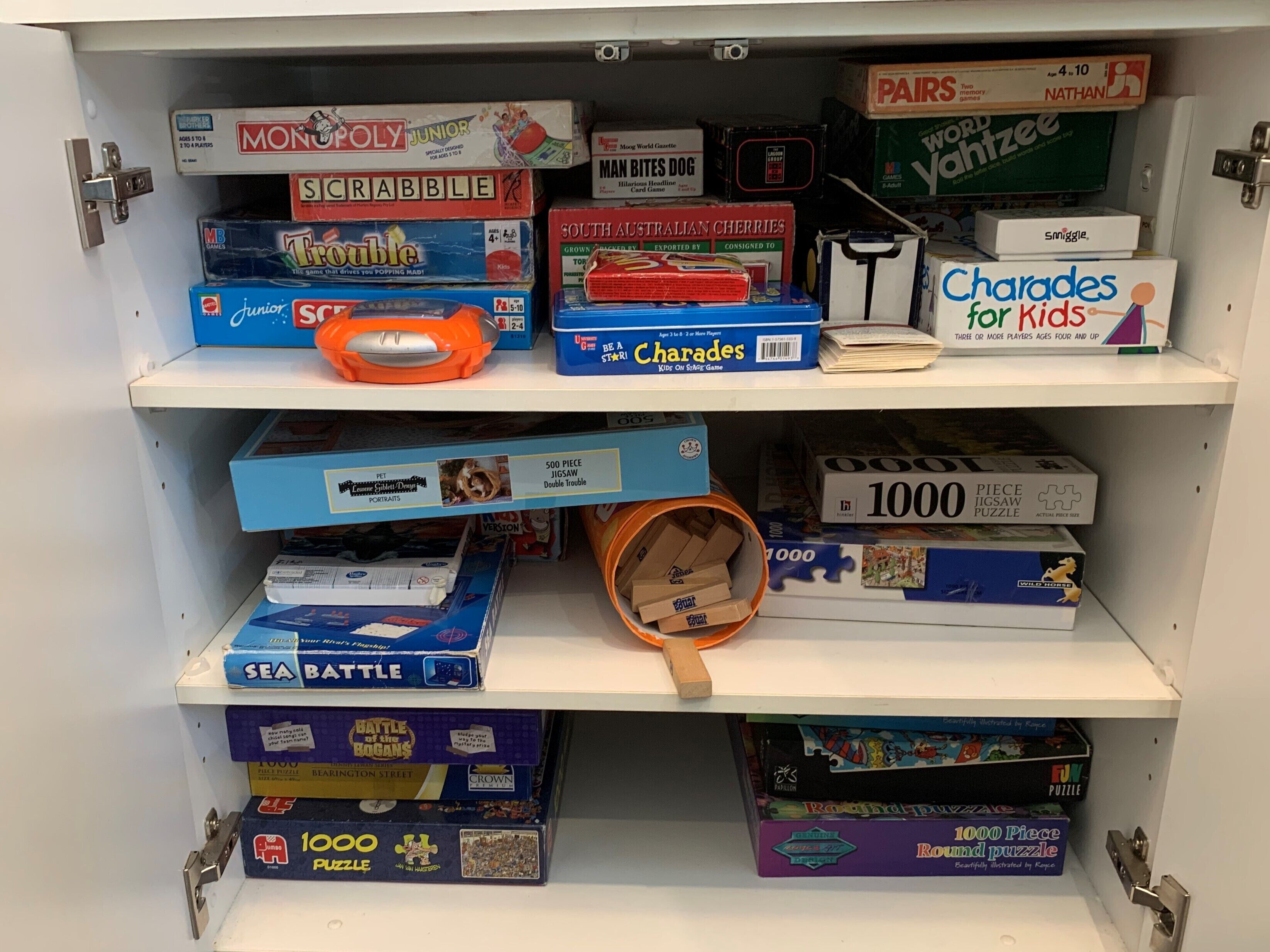 A shelf with various board games including Monopoly Junior, Scrabble, and Charades for Kids.