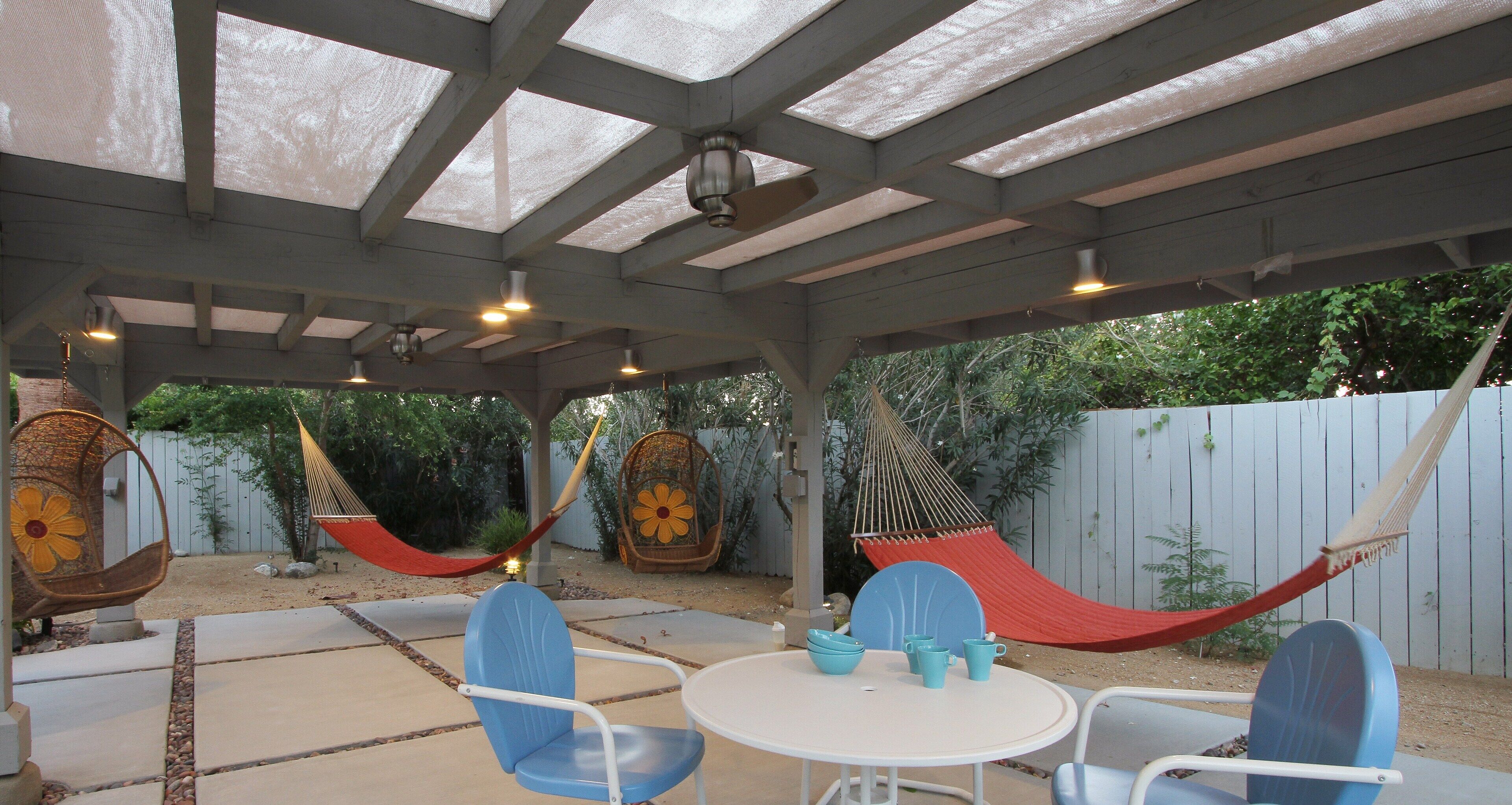 Un patio couvert avec une table et des chaises, des hamacs et une clôture en bois en arrière-plan.