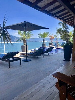 Une terrasse avec des chaises longues, une piscine et une vue sur la mer.