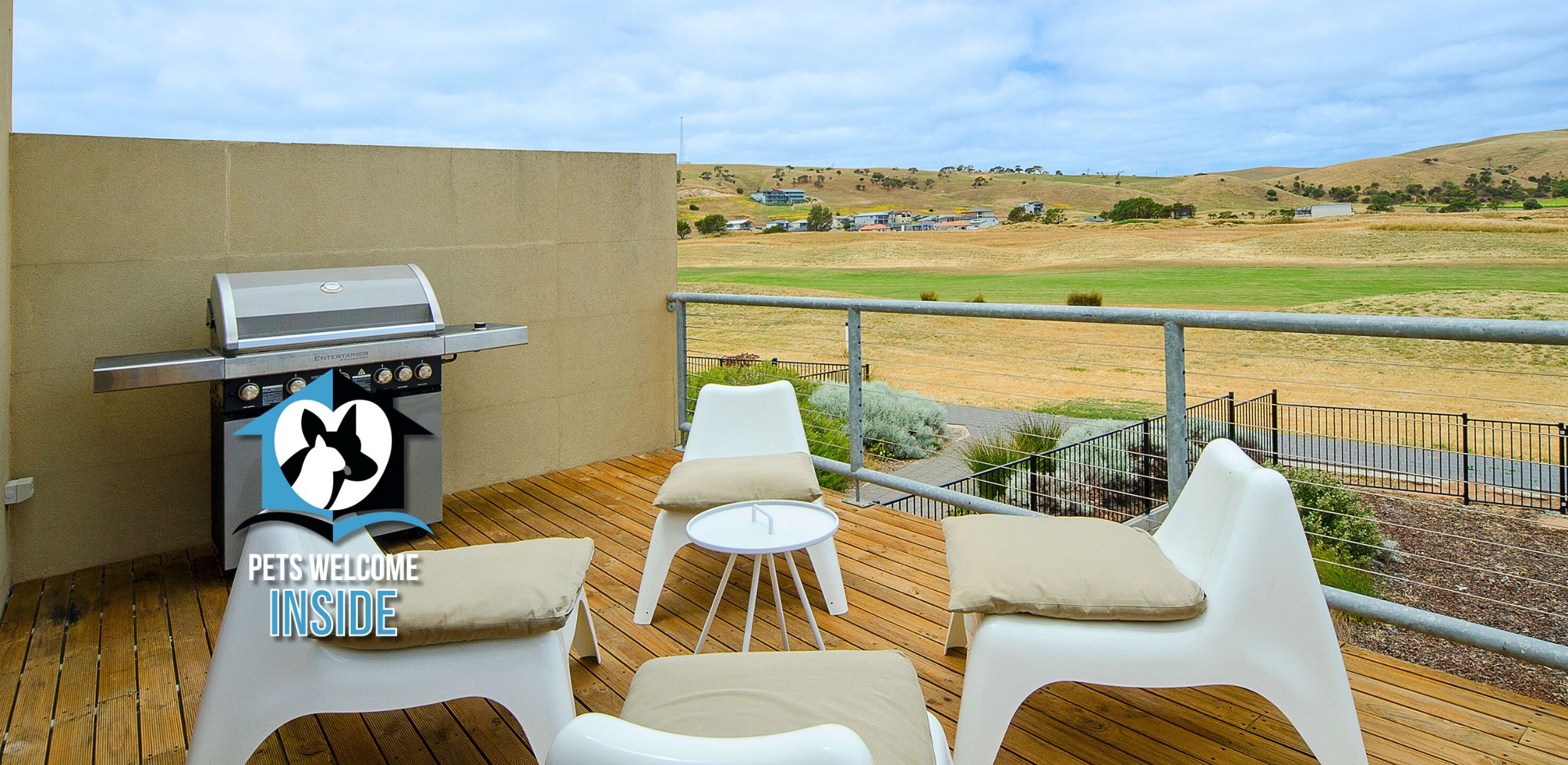 Une terrasse extérieure avec un barbecue, deux chaises en plastique blanches et une petite table ronde.