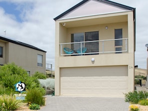 A two-story house with a balcony, a garage, and a garden with plants and flowers.