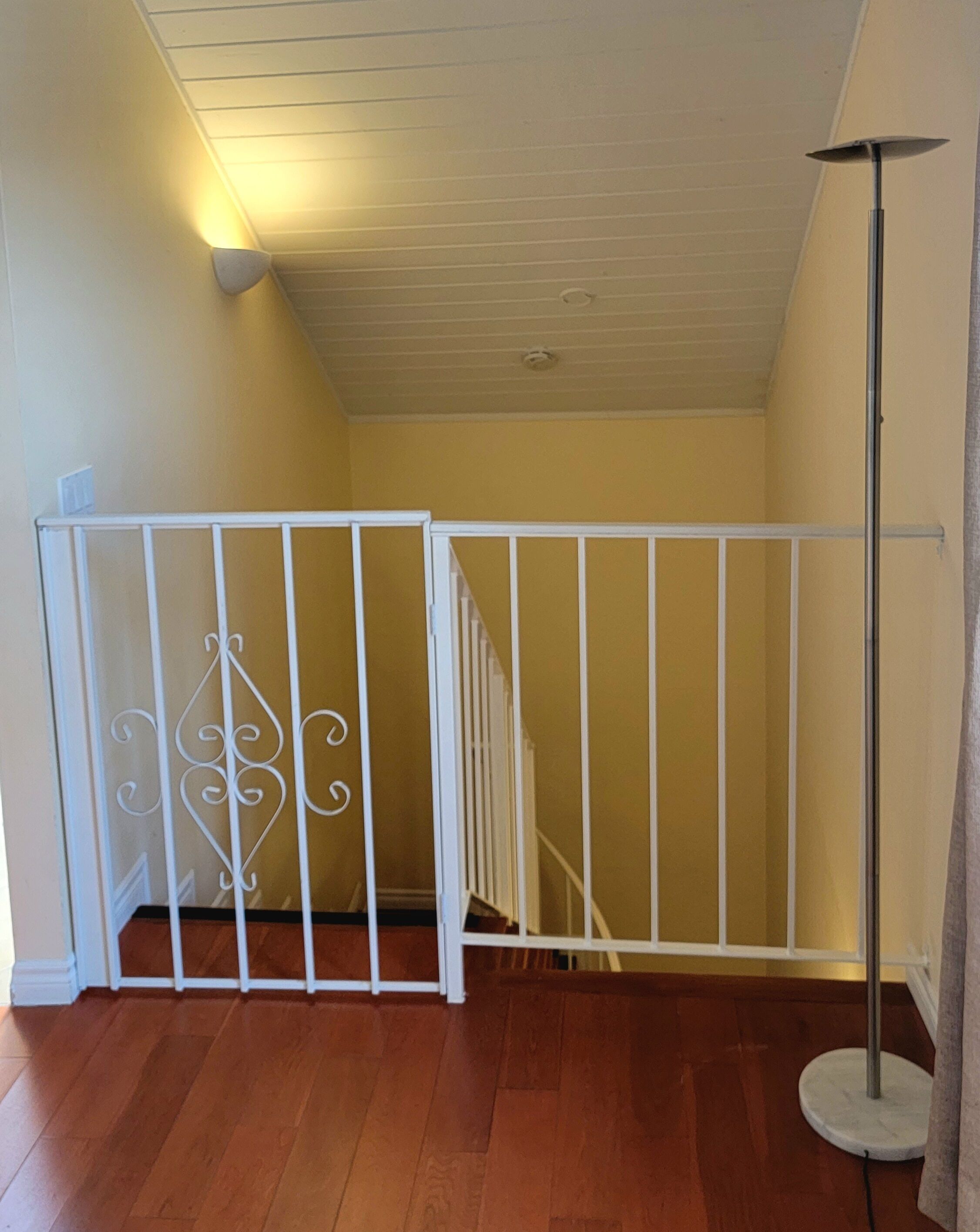 A staircase with a white railing, a white floor lamp, and a ceiling with recessed lighting.