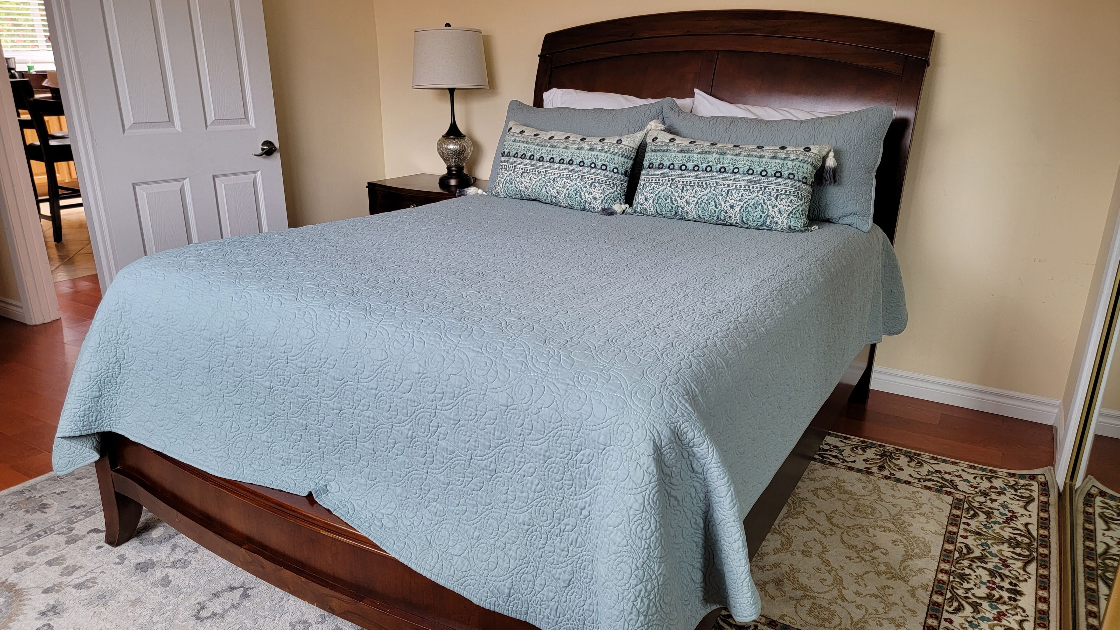 A bedroom with a bed, a nightstand, a lamp, and a patterned rug.