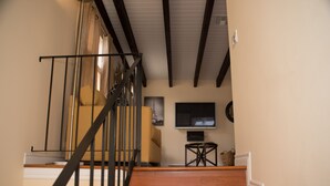 Un escalier en bois, doté d’une rampe noire, mène à un palier. Un téléviseur est fixé au mur, au-dessus du palier.