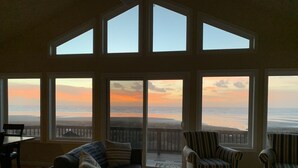 A spacious living room with a large view of the ocean at sunset, featuring a sofa, armchairs, and a coffee table. - Oceanfront Beach House-Nestled on the N. Beach of the Washington Coast (Moclips)