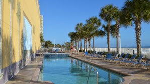 Ein Swimmingpool mit Liegestühlen und Palmen, umgeben von einem Gebäude mit Wandgemälde.