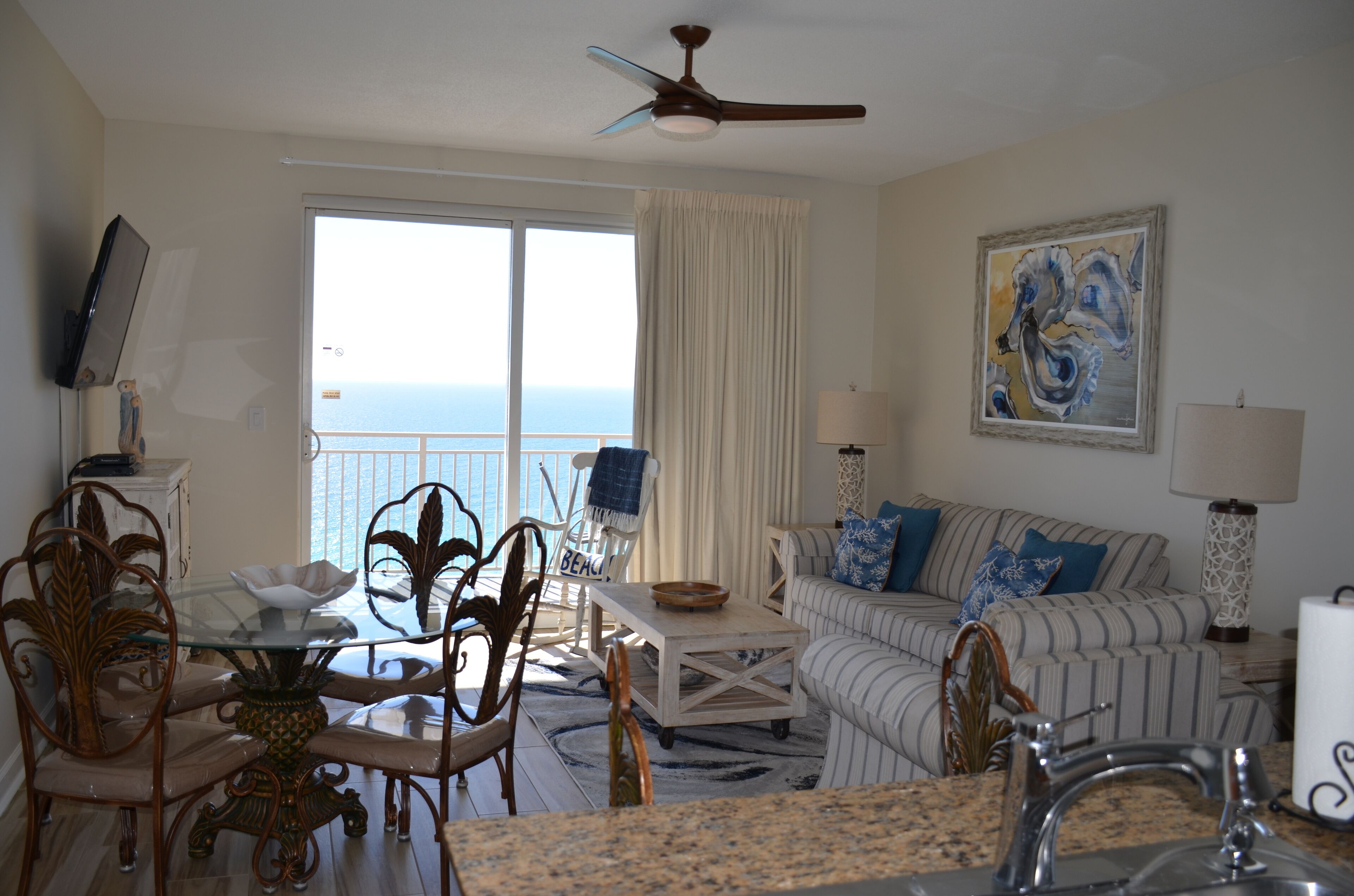 A room with a dining table, chairs, a sofa, a TV, and a view of the ocean.