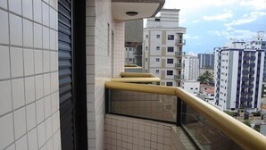 Ein schmaler Balkon mit Glastrennwand und Fliesenboden, mit Blick auf eine Stadtlandschaft mit mehreren Gebäuden.