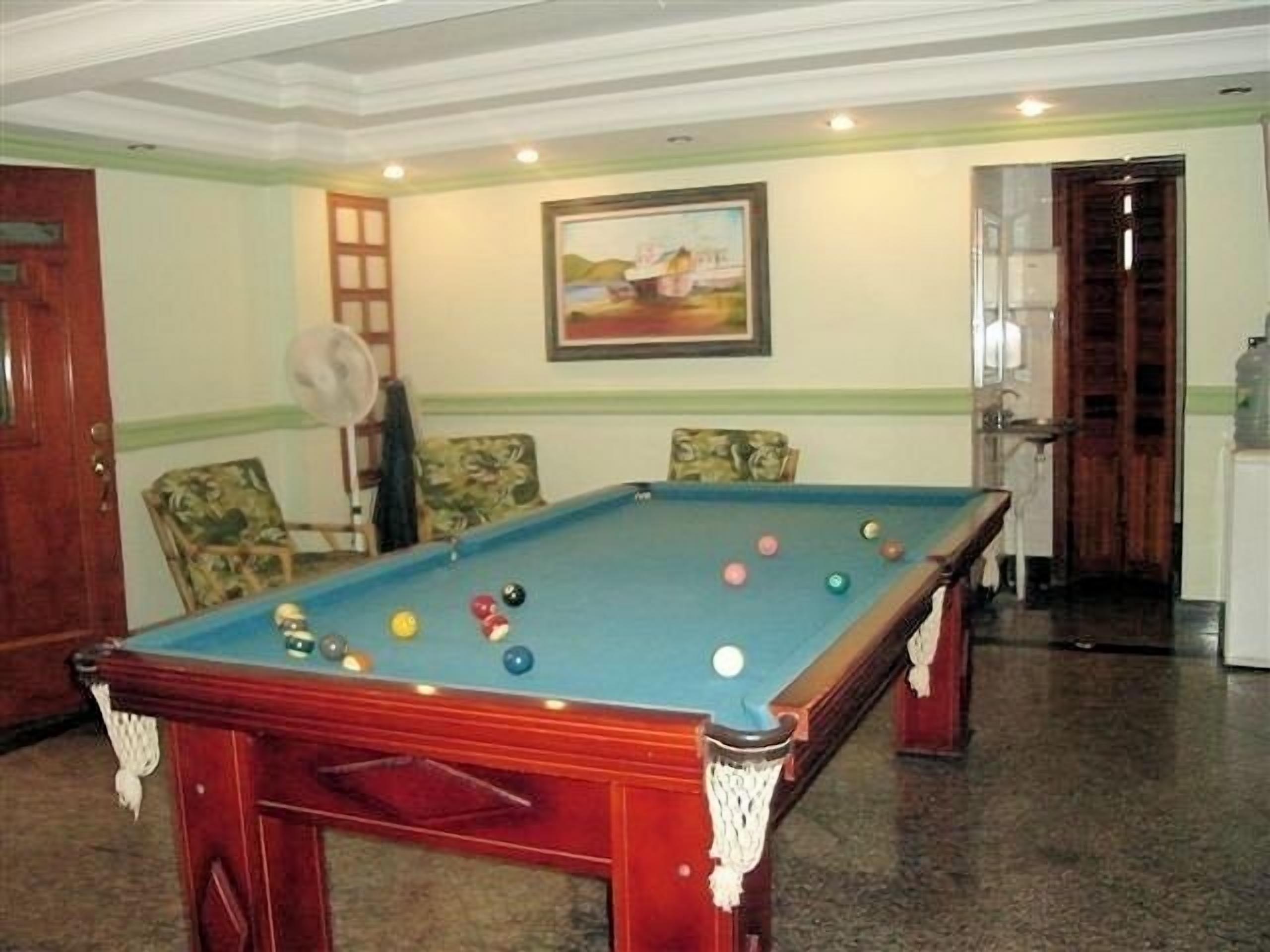 A pool table with balls, a fan, and a painting on the wall.