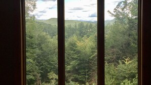 A window with a view of a dense forest and hills in the distance. - Luxurious, Secluded, Ski Chalet, w/ Country Decor & Hot Tub Near Okemo (Ludlow)