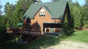 A wooden cabin with a green roof, a deck, and a garage. - Luxurious, Secluded, Ski Chalet, w/ Country Decor & Hot Tub Near Okemo (Ludlow)