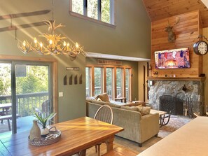 A cozy living room with a fireplace, a wooden ceiling, and a large window overlooking a deck. - Luxurious, Secluded, Ski Chalet, w/ Country Decor & Hot Tub Near Okemo (Ludlow)