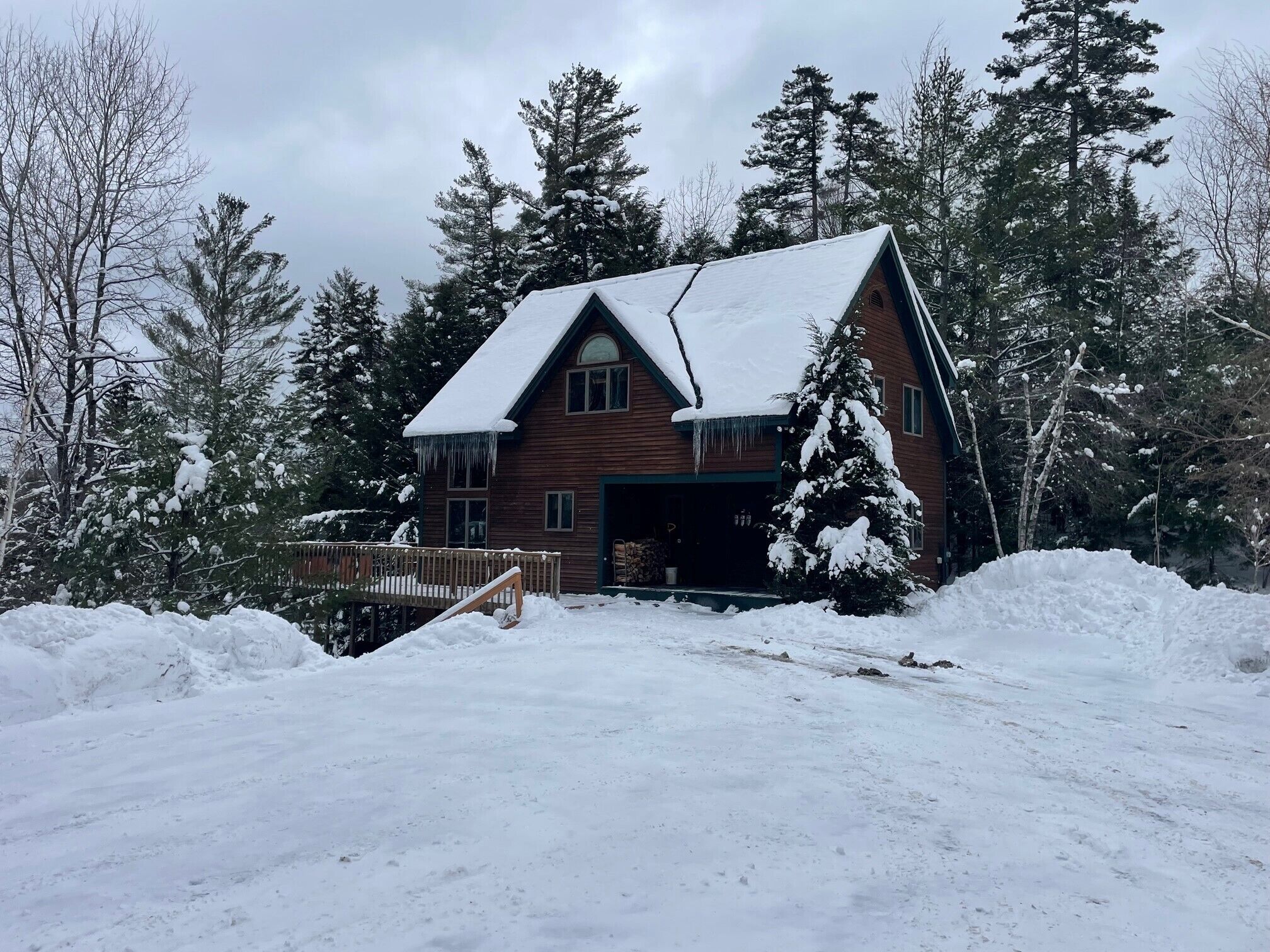 A wooden cabin with a steeply pitched roof, surrounded by snow-covered trees and a wooden deck.