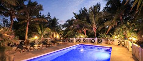 Une piscine entourée d’une clôture blanche, avec des palmiers en arrière-plan.