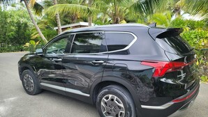 A black SUV parked on a road with palm trees in the background.