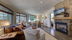 A spacious living room with a fireplace, a television mounted on the wall, and a cozy seating area with a sofa and chairs.