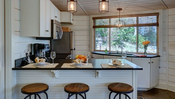 A kitchen with white cabinets, a central island with stools, a coffee maker, and hanging pendant lights.