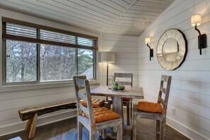 A dining area with a wooden table, chairs, a bench, and a large window with blinds.