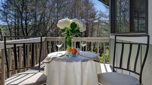 A table set on a balcony with a white tablecloth, a vase with white flowers, and two wine glasses.