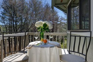 Una mesa con mantel blanco, un florero con flores y dos copas de vino en un balcón con barandilla.
