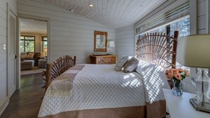 A bedroom with a large bed, wooden headboard, bedside table, and a window with blinds.