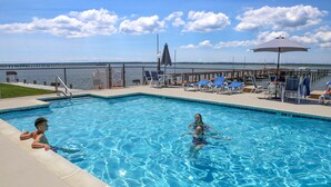 Ein Pool mit Blick auf das Wasser, eine Sonnenterrasse mit Liegestühlen und ein Zaun.
