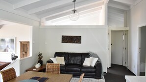 A modern living room with a black leather sofa, a glass ceiling, and a decorative wall piece. - Holiday home at Lake Tarawera, Rotorua (Lake Tarawera)