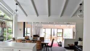 A spacious living area with a dining table, wicker chairs, a black leather sofa, and a large window providing a view of the outdoors. - Holiday home at Lake Tarawera, Rotorua (Lake Tarawera)
