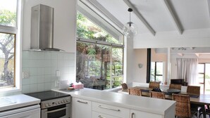 A modern kitchen with white cabinetry, a built-in oven, and a large window overlooking a garden. - Holiday home at Lake Tarawera, Rotorua (Lake Tarawera)
