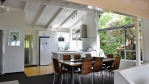 A modern kitchen with white cabinetry, a central island, and a dining area with wicker chairs. - Holiday home at Lake Tarawera, Rotorua (Lake Tarawera)