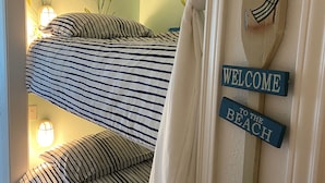 A bunk bed with striped bedding, a 'WELCOME TO THE BEACH' sign, and a palm tree decoration. - One Bedroom Oceanfront Condo With Room for Six (South Padre Island)