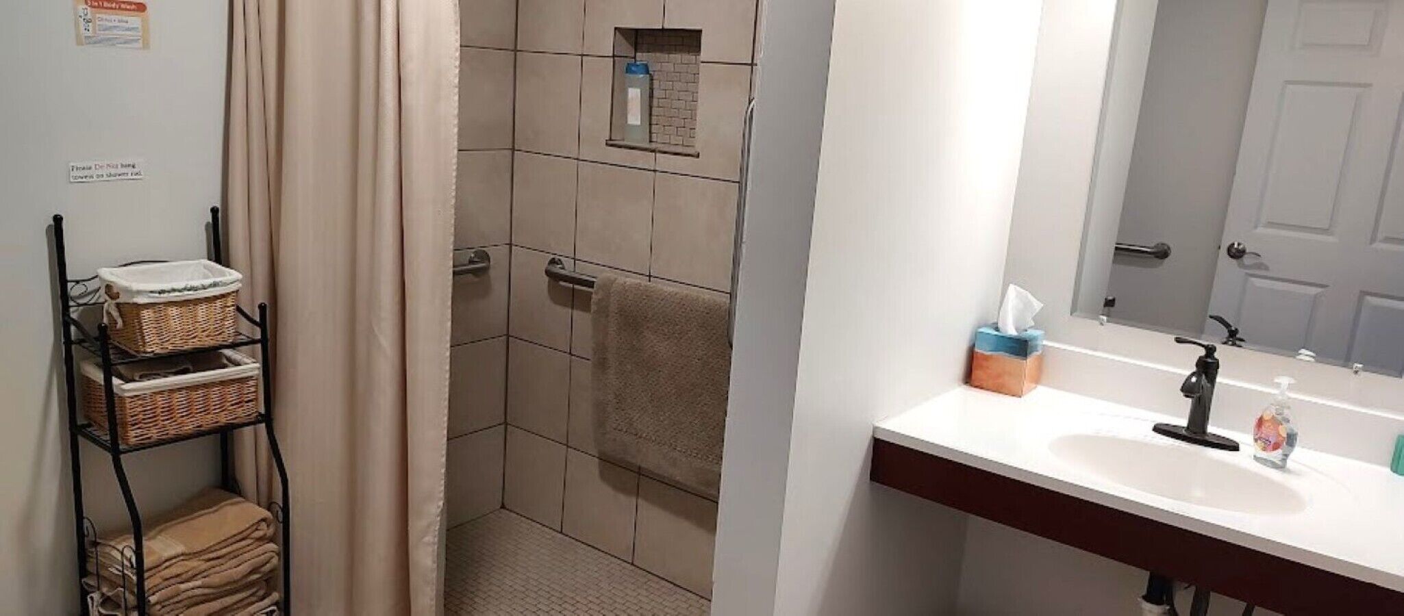 A bathroom with a shower, a sink with a mirror, and a towel rack.
