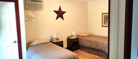 A room with two single beds, a star decoration on the wall, an air conditioning unit, and a framed picture.