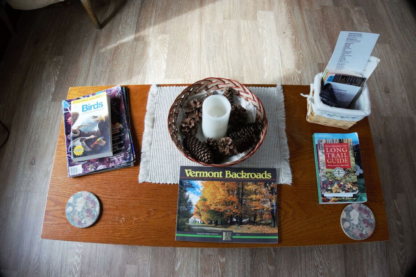 Une table en bois sur laquelle se trouvent un livre intitulé « Vermont Backroads », une tasse de café, un panier rempli de pommes de pin et un guide de randonnée intitulé « Long Trail Guide ».