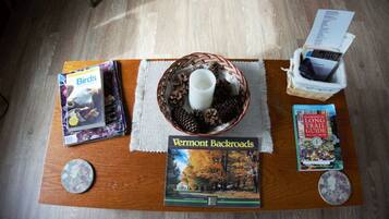 Une table en bois sur laquelle se trouvent un livre intitulé « Vermont Backroads », une tasse de café, un panier rempli de pommes de pin et un guide de randonnée intitulé « Long Trail Guide ».