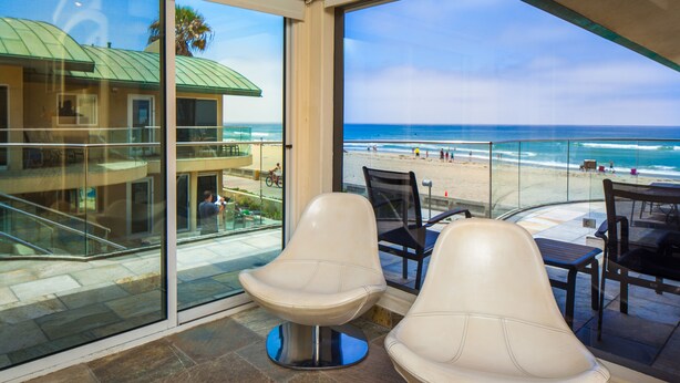 Ein Balkon mit zwei weißen Stühlen, einer Glastrennwand und Blick auf Strand und Meer.