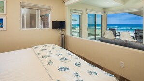 Ein Schlafzimmer mit Bett, Fernseher und einem Balkon mit Blick auf den Strand.