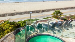 Ein Poolbereich mit Glasgeländern, Liegestühlen und Blick auf Strand und Meer.