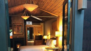 A cozy bedroom with a bed, a small table, two lamps, a colorful rug, and a fireplace.