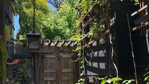A narrow stone pathway leading to a wooden gate in a lush garden area with various plants and a hanging lantern.