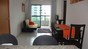 A living room with a sofa, a dining table with chairs, and a view through a large window. - Modern apartment, beautifully decorated and furnished, with swimming pool and Wi-Fi. (Recife)