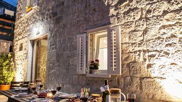 Un espace extérieur aménagé pour les repas, avec un bâtiment en pierre, une table en bois et des chaises.