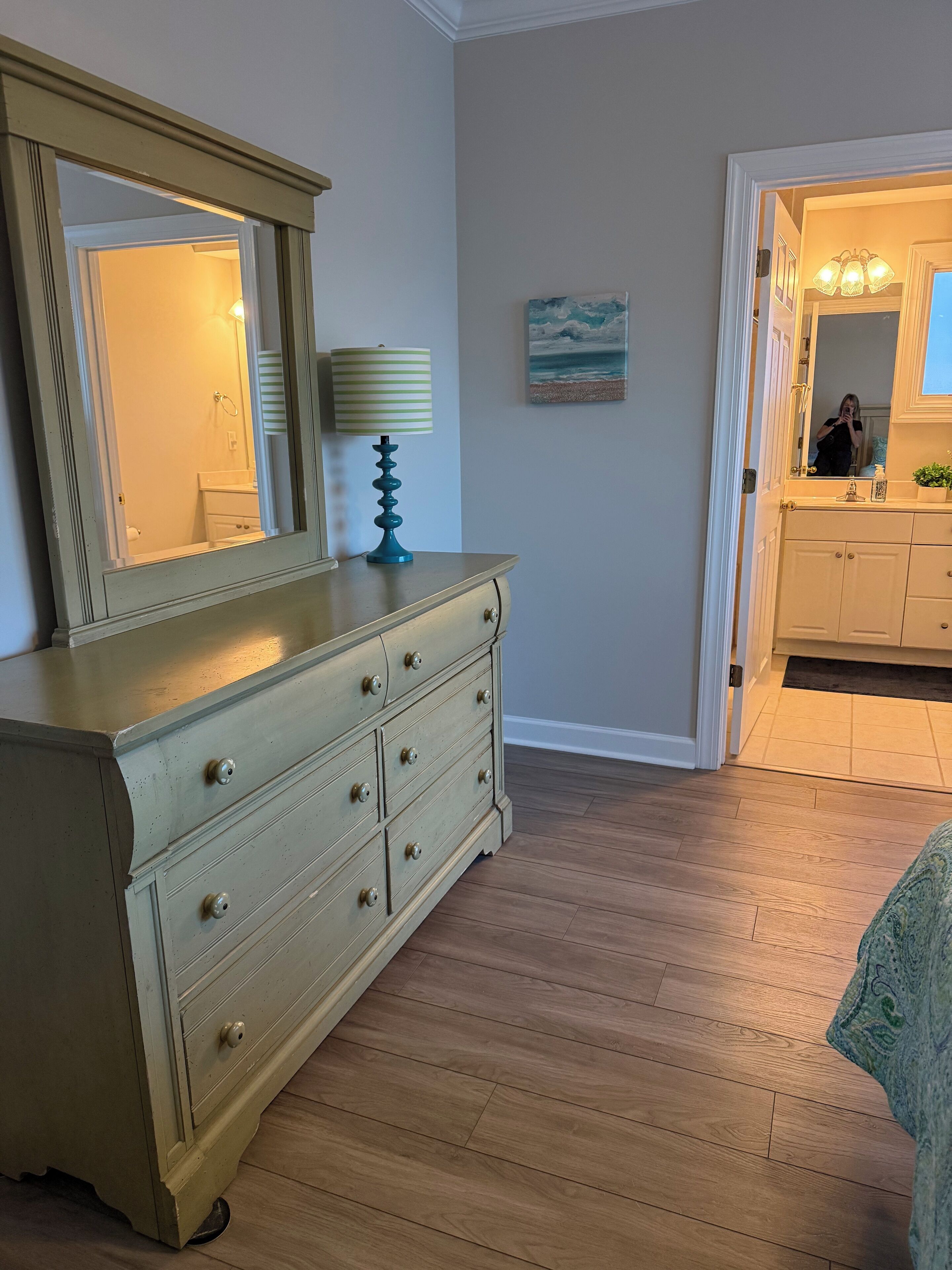 A room with a dresser, a mirror, a lamp, and a painting on the wall.