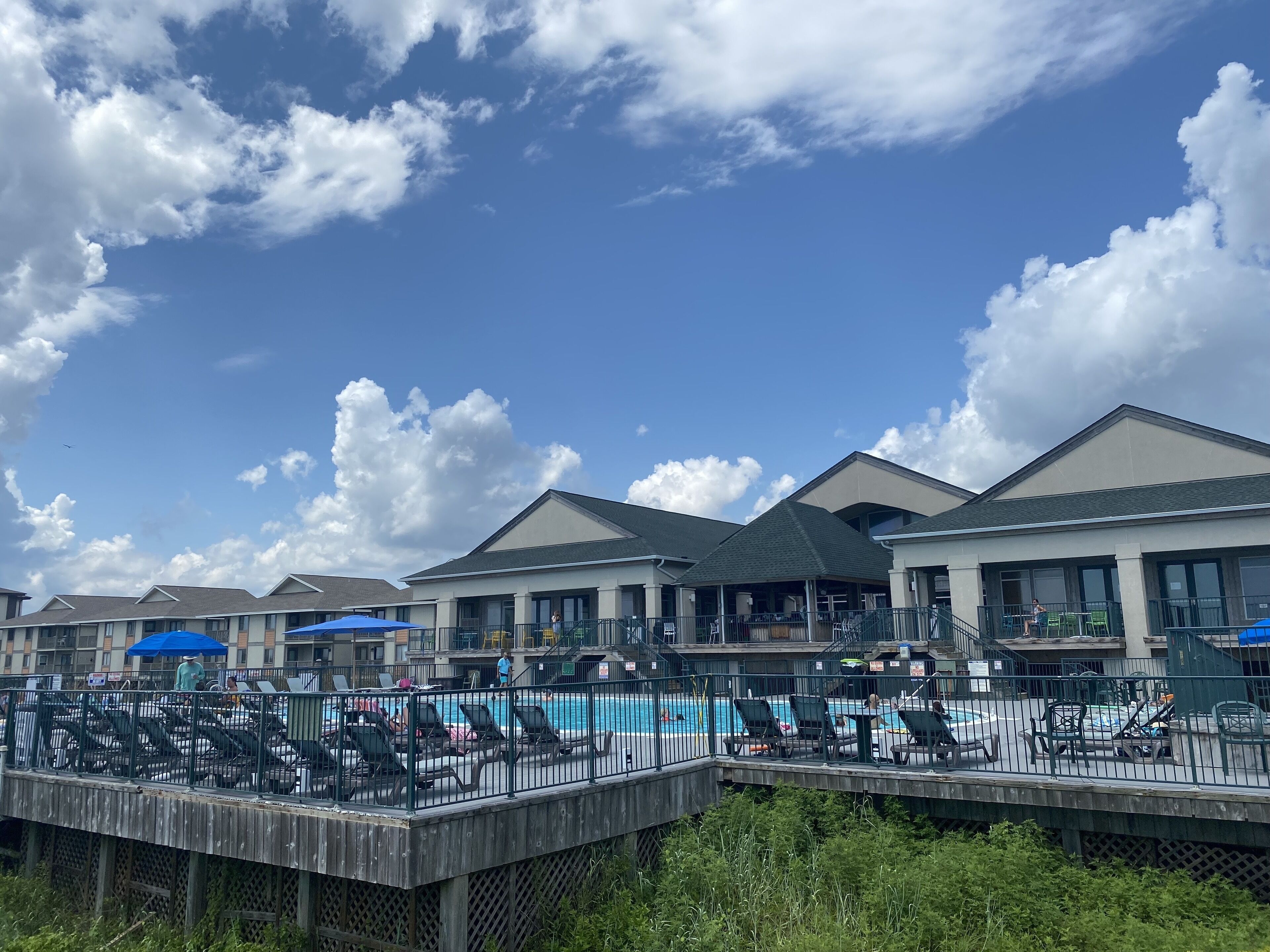 A pool area with lounge chairs and umbrellas, surrounded by buildings with large windows and a clear sky.