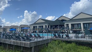 A pool area with lounge chairs and umbrellas, surrounded by buildings with large windows and a clear sky. - Condo with AMAZING Ocean View! Labor Day Weekend is available and discounted ! (Ocean Isle Beach)