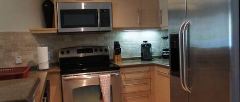 A modern kitchen with stainless steel appliances, wooden cabinets, and a tiled backsplash.