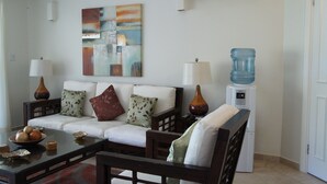 Ein Wohnzimmer mit einem weißen Sofa, zwei Beistelltischen mit Lampen, einem Couchtisch mit dekorativen Gegenständen und einem großen abstrakten Gemälde an der Wand.