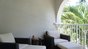 Ein Balkon mit Korbmöbeln, einem kleinen Tisch und Blick auf Palmen.