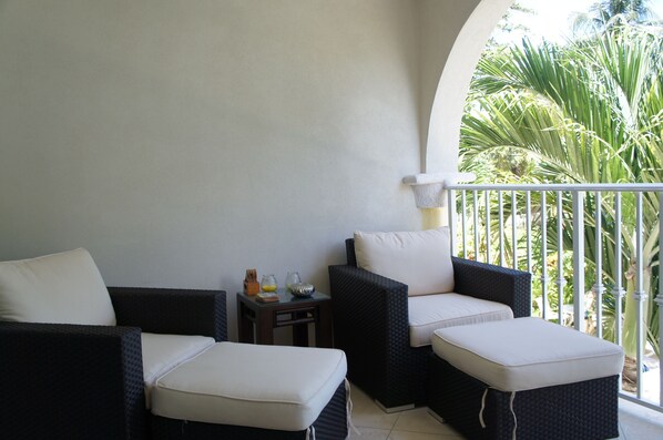 A balcony with wicker furniture, a small table, and a view of palm trees.
