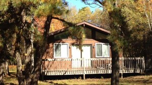 A cabin with a wooden deck and a fenced area, surrounded by trees.
